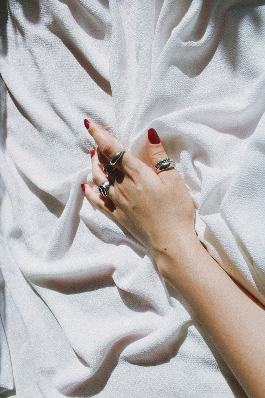 A manicured hand adorned with silver rings rests gracefully on white linen.