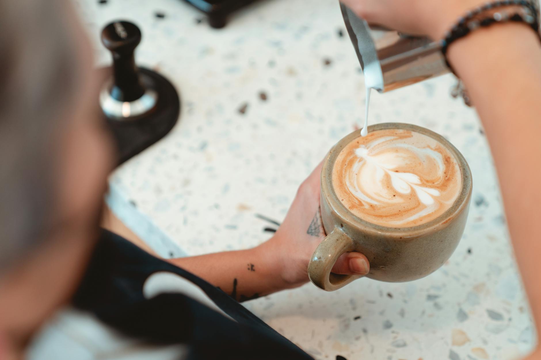 Barista pouring latte art into a ceramic cup on a marble counter at Olen Coffee.